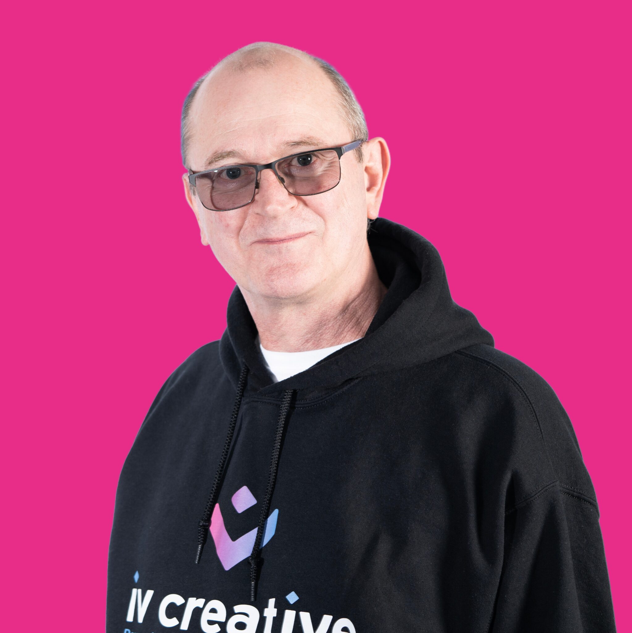 A portrait shot of a man in a black hoodie on a pink background.